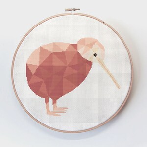 May include: A cross-stitch embroidery hoop with a geometric design of a kiwi bird in shades of pink and brown.