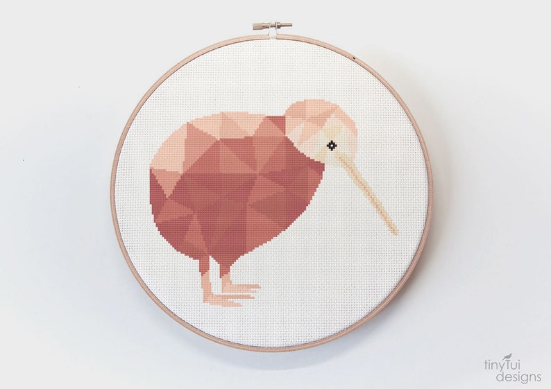 May include: A cross-stitch embroidery hoop with a geometric design of a kiwi bird in shades of pink and brown.