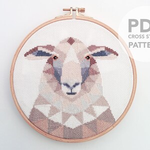 Puede incluir: Un patr&oacute;n de punto de cruz de la cara de una oveja en un aro de bordado de madera. La oveja tiene pelaje marr&oacute;n, blanco y gris. El patr&oacute;n est&aacute; disponible para descargar en PDF. "PDF CROSS STITCH PATTERN" est&aacute; escrito en gris sobre un c&iacute;rculo blanco.