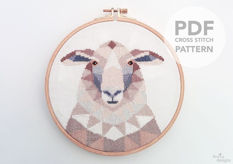 Puede incluir: Un patr&oacute;n de punto de cruz de la cara de una oveja en un aro de bordado de madera. La oveja tiene pelaje marr&oacute;n, blanco y gris. El patr&oacute;n est&aacute; disponible para descargar en PDF. "PDF CROSS STITCH PATTERN" est&aacute; escrito en gris sobre un c&iacute;rculo blanco.
