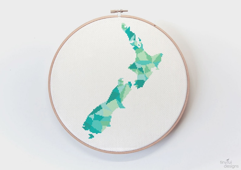May include: A cross-stitch embroidery hoop with a green and blue geometric design of the outline of New Zealand.