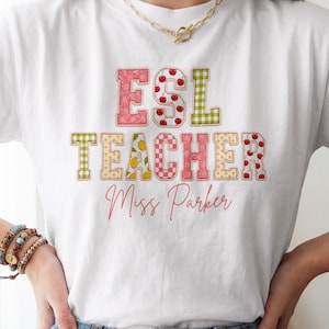 May include: A white short-sleeve t-shirt featuring the text ESL TEACHER in block letters with various colorful patterns including cherries, lemons, and gingham. Below the main text, the name Miss Parker is printed in a cursive red script font.