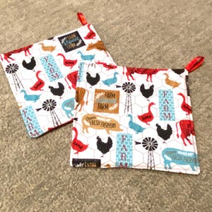 May include: Two white square pot holders with a farm-themed pattern. The pattern includes images of chickens, cows, geese, and windmills in red, black, brown, and blue. The text "Farm Fresh Everyday" and "Farm" is also visible. Each pot holder has a red loop.