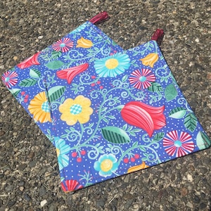 May include: Two blue pot holders with a floral pattern in shades of red, yellow, and green. The pot holders have a white background with a blue polka dot pattern.