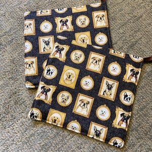 May include: Two black and gold kitchen pot holders with a pattern of dogs in frames. The dogs are different breeds and are in various poses.
