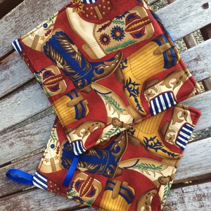 Puede incluir: Dos agarraderas de olla de tela roja con un patrón de botas de vaquero azules, blancas y amarillas. Las agarraderas tienen un ribete azul y blanco.