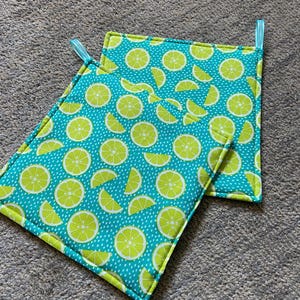 May include: Two turquoise blue pot holders with a lime slice pattern. The pot holders have a light blue hanging loop.