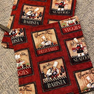 May include: Two red and beige kitchen pot holders with a chef theme. The pot holders feature a variety of images including a chef making coffee, a chef preparing seafood, a chef preparing vegetables, and a chef preparing a meal. The pot holders also feature the words "Delectable", "Barista", "Seafood", "Veggies", and "Savour the Flavor".