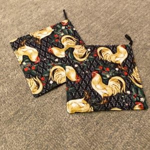 May include: Two square pot holders with a black background and a repeating pattern of yellow roosters, red berries, and green leaves. Each pot holder has a small black loop for hanging.