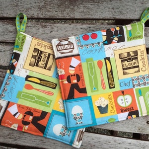 May include: Two colourful kitchen potholders with a patchwork design. The design includes images of cooking utensils, food items, and text like "Sugar", "Flour", and "Kiss the Cook". Each potholder has a green loop.