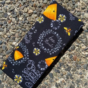 May include: Black fabric with a bee theme. The fabric has a repeating pattern of honeycombs, bees, flowers, and the text "Bee Kind" and "Be Yourself".