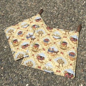 Puede incluir: Dos agarraderas cuadradas con un estampado de escena de granja. La tela presenta graneros rojos, carruajes tirados por caballos, manzanos y gansos sobre un fondo amarillo claro. Cada agarradera tiene un lazo marrón para colgar.