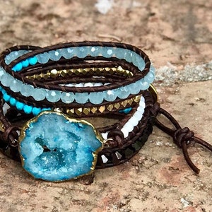 May include: A multi-strand leather wrap bracelet with turquoise and gold beads, a large blue agate stone, and a brown leather tie closure.