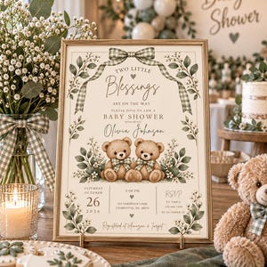 May include: A rectangular baby shower invitation sign in a gold frame featuring two teddy bears, green gingham bows, and botanical illustrations. The text reads: Two Little Blessings Are On The Way, Please Join Us For A Baby Shower Honoring Olivia Johnson.