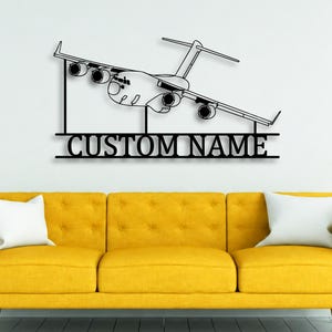 Pode incluir: Uma peça de arte de parede em metal preto com o contorno detalhado de um avião de carga com quatro motores. Abaixo da aeronave, uma barra horizontal exibe o texto CUSTOM NAME em uma fonte serifada em negrito e letras maiúsculas.
