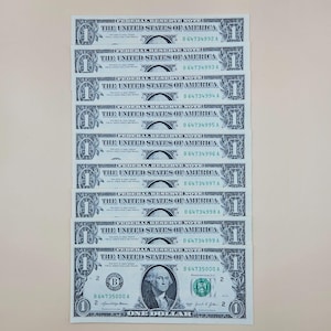 May include: A vertical stack of ten sequential one-dollar bills from the United States of America. Each note features the text Federal Reserve Note, The United States of America, and serial numbers ranging from B 64734992 A to B 64735000 A.