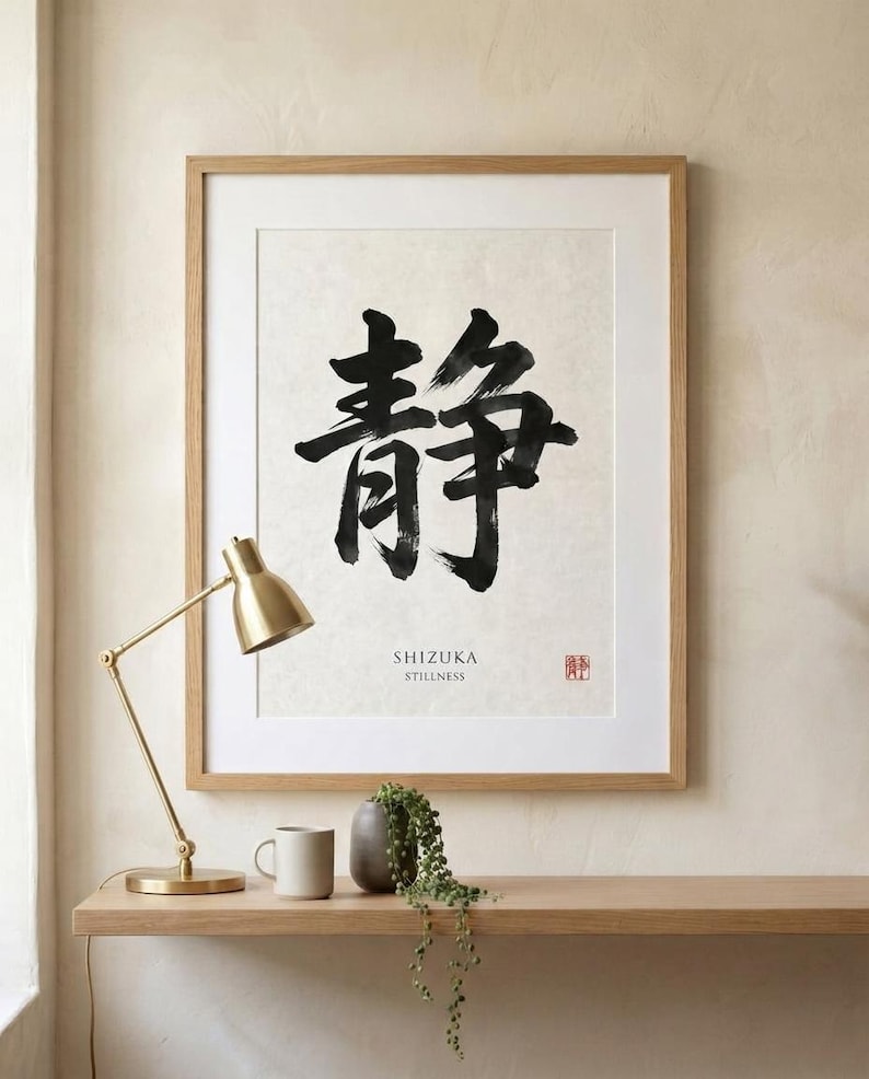A framed wall art print featuring large black Japanese calligraphy characters on a textured off-white background. Below the characters, the text reads SHIZUKA STILLNESS, accompanied by a small red square stamp in the bottom right corner.