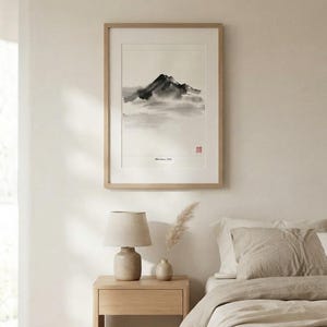 A framed wall art print featuring a black and white ink wash painting of a mountain peak with soft, hazy clouds. The artwork includes the text "Mountain, Mist" and a small red square stamp, all encased in a light wood frame.