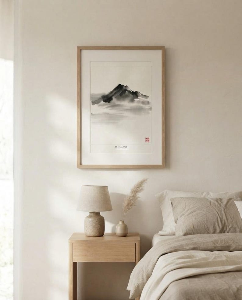 A framed wall art print featuring a black and white ink wash painting of a mountain peak with soft, hazy clouds. The artwork includes the text "Mountain, Mist" and a small red square stamp, all encased in a light wood frame.
