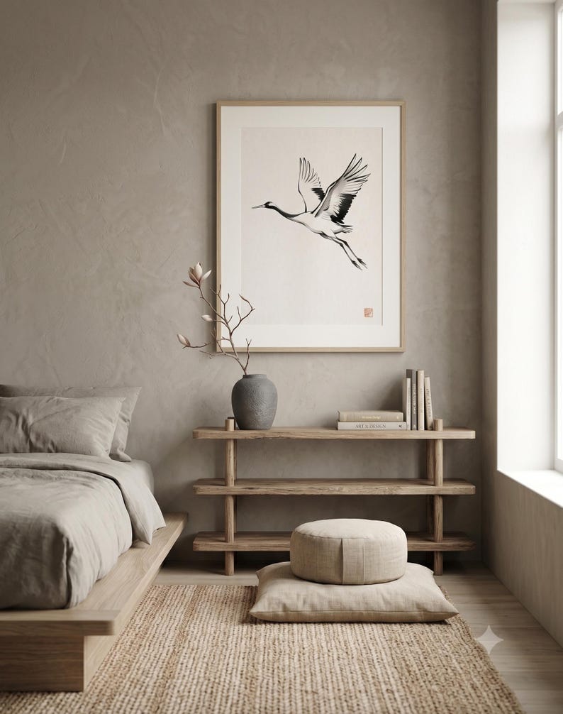 Sumi-e crane print framed in oak, seen on three quiet walls — above a linen bed, on a gallery wall and above an oak console.