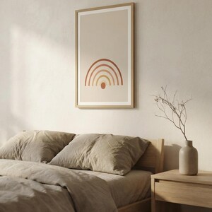 May include: A framed vertical wall art print featuring a minimalist rainbow graphic with concentric arches in shades of terracotta, orange, and yellow, centered above a small solid circle on a light beige background, enclosed in a light wood frame.