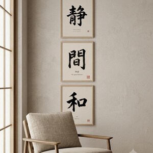 Op de afbeelding: Drie vierkante ingelijste kunstwerken verticaal gerangschikt, elk met zwarte Japanse kalligrafie op een cr&egrave;mekleurige achtergrond. De bovenste print toont het teken voor stilte, de middelste voor de tussenruimte en de onderste voor harmonie.
