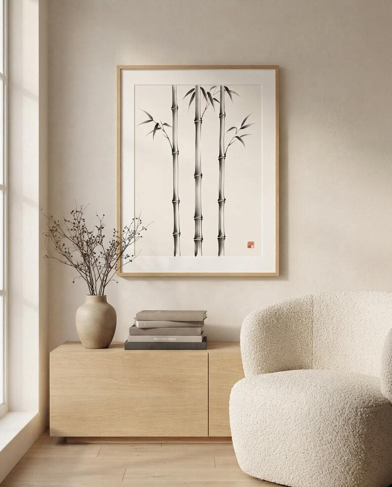 A framed wall art print featuring a black and white ink wash illustration of three bamboo stalks with leaves, set against a cream background, with a small red square seal mark in the lower right corner of the artwork.