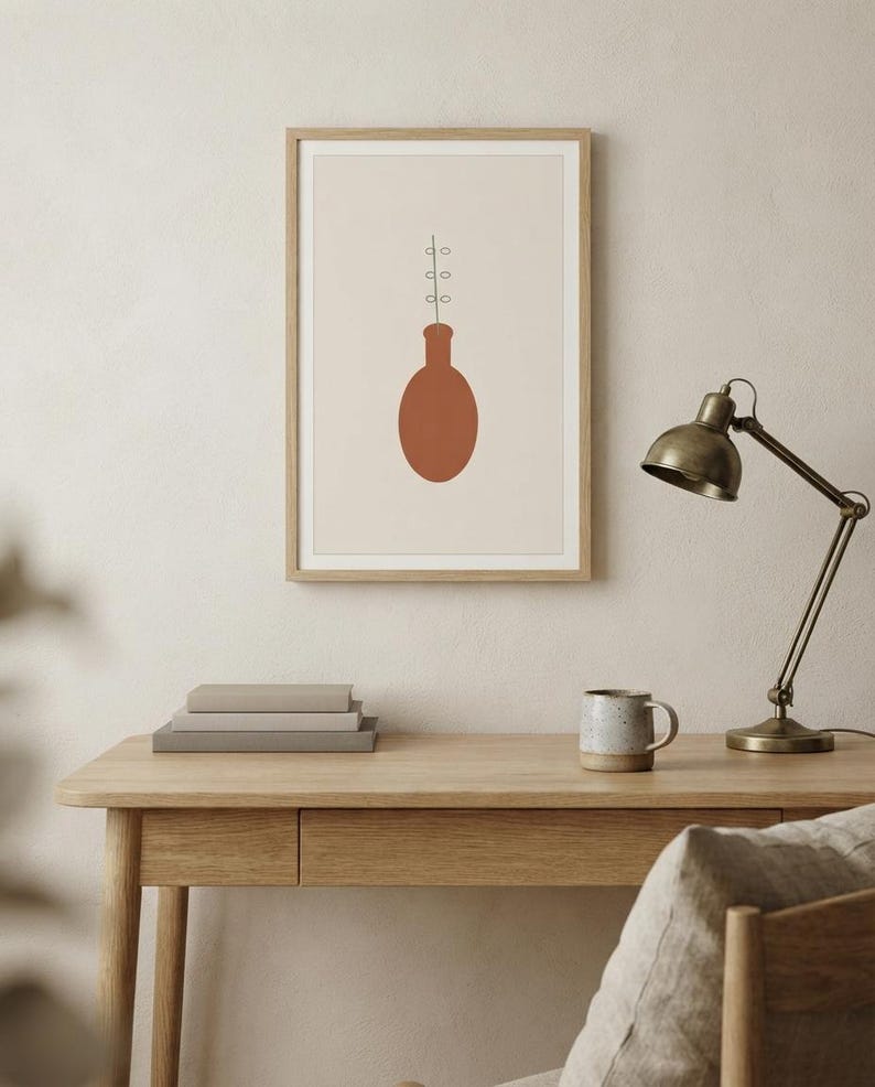 May include: A framed wall art print featuring a solid terracotta-colored oval vase shape centered on a light beige background. A thin black line extends upward from the vase, displaying three pairs of small, simple, outlined circular leaves.