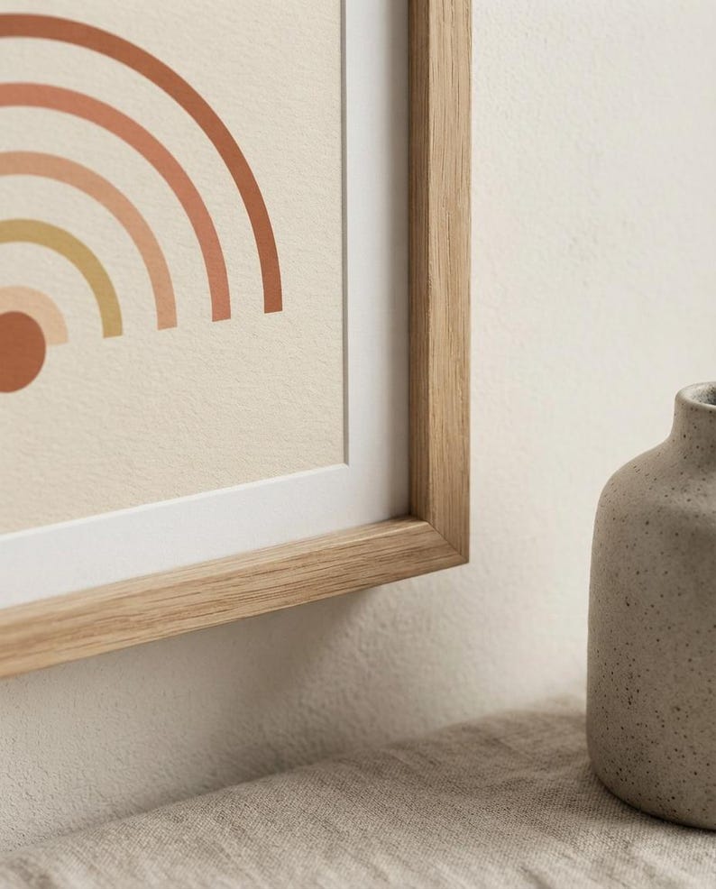 May include: A framed print featuring a partial graphic of a rainbow with concentric arches in shades of terracotta, peach, and mustard yellow on a cream background, encased in a light-toned wooden frame with a white mat border.
