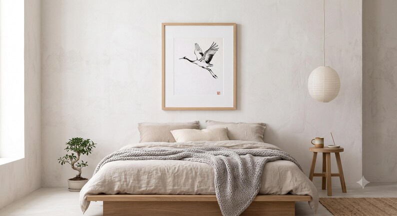 Sumi-e crane print framed in oak, seen on three quiet walls — above a linen bed, on a gallery wall and above an oak console.