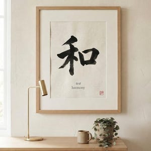 A framed wall art print featuring the black Japanese kanji character for harmony, which is 'wa', printed on off-white paper. Below the large character, the text 'wa' and 'harmony' appear in a small font, with a red stamp in the corner.