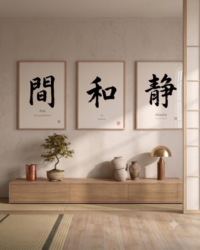 Op de afbeelding: Drie ingelijste wandkunstprints met zwarte Japanse kalligrafiekarakters en Engelse tekst. De linkerprint toont 'ma' en 'the space between', de middelste 'wa' en 'harmony', en de rechter 'shizuka' en 'STILLNESS' op wit papier.