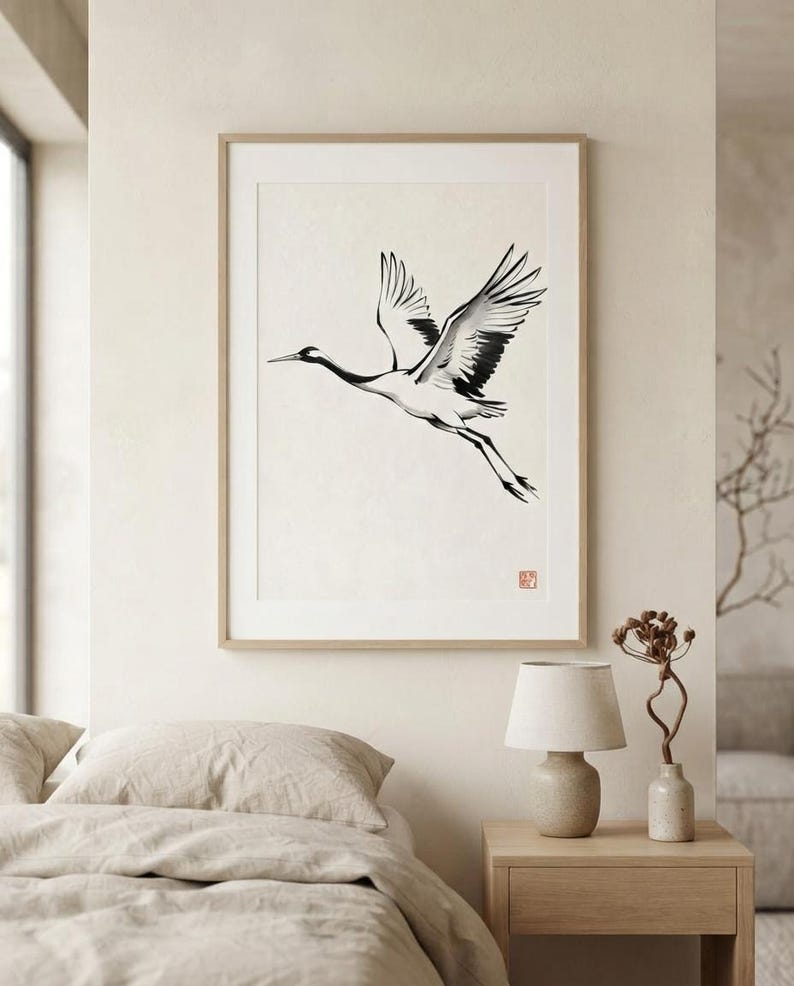 Sumi-e crane print framed in oak, seen on three quiet walls — above a linen bed, on a gallery wall and above an oak console.