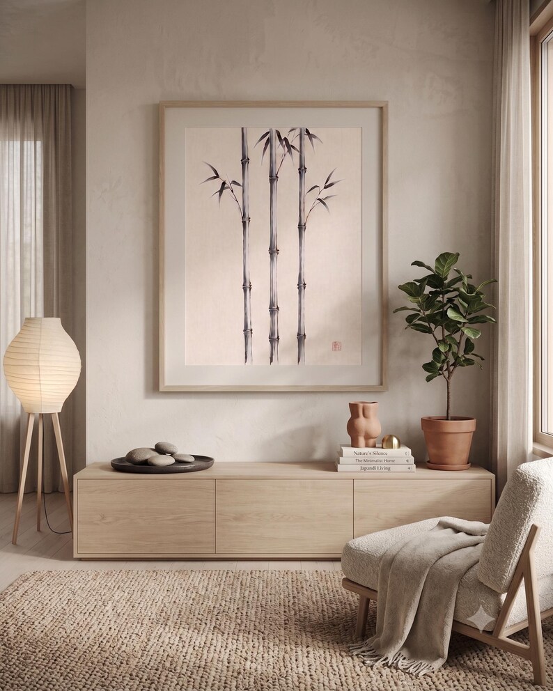 Pode incluir: Uma impress&atilde;o de arte emoldurada com uma ilustra&ccedil;&atilde;o a tinta preta de tr&ecirc;s caules de bambu num fundo bege claro. A obra de arte &eacute; apresentada numa moldura de madeira clara e est&aacute; pendurada centrada numa parede sobre um m&oacute;vel de madeira.