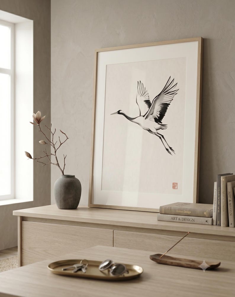 Sumi-e crane print framed in oak, seen on three quiet walls — above a linen bed, on a gallery wall and above an oak console.