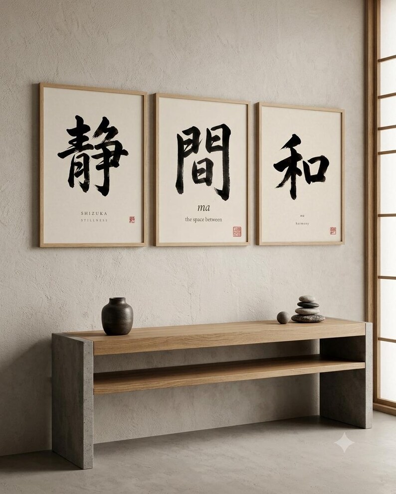 Op de afbeelding: Drie ingelijste wandkunstwerken met zwarte Japanse kalligrafie op een gebroken witte achtergrond. De prints tonen de woorden SHIZUKA, ma en wa met hun Engelse vertalingen eronder. Onder de kunstwerken staat een lange houten consoletafel.