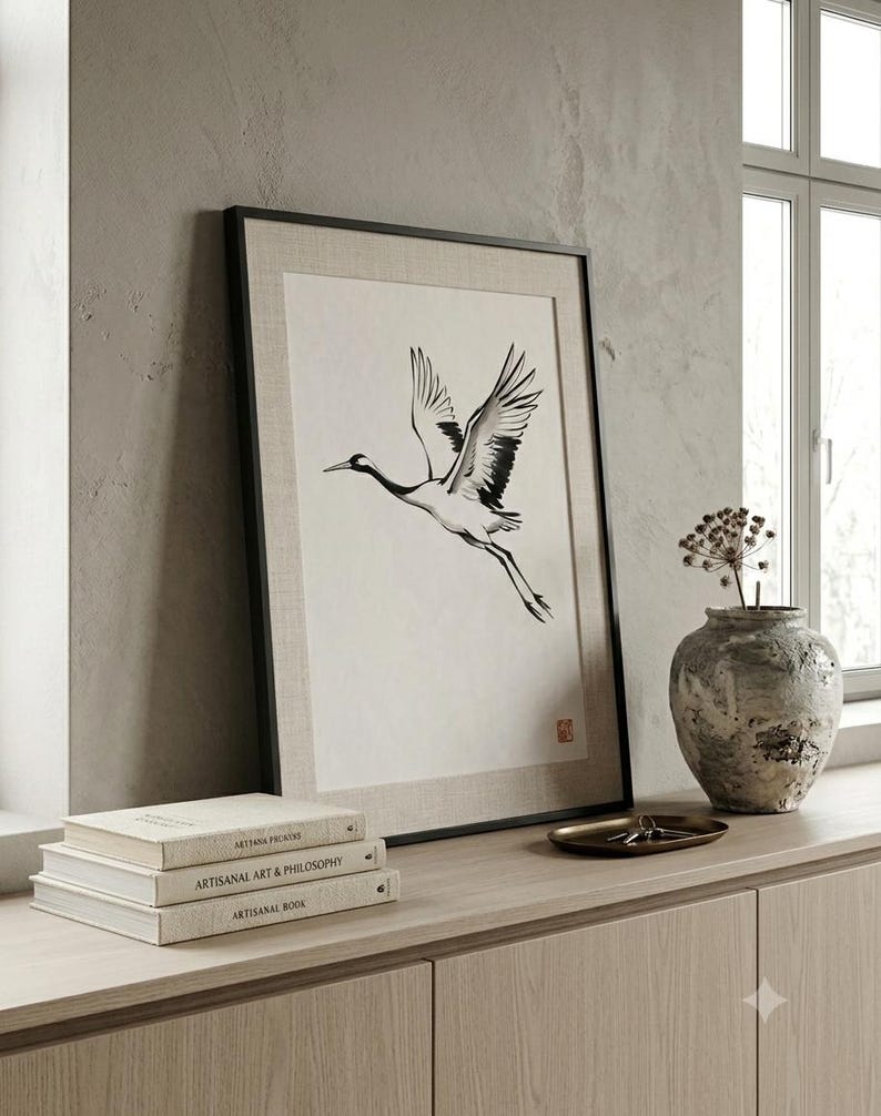 Sumi-e crane print framed in oak, seen on three quiet walls — above a linen bed, on a gallery wall and above an oak console.