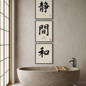 Op de afbeelding: Drie vierkante wandkunstprints in zwarte lijsten met zwarte Japanse kalligrafie op een cr&egrave;mekleurige achtergrond. De bovenste print toont het teken voor Shizuka, de middelste voor ma en de onderste voor wa, elk met kleine rode stempels.