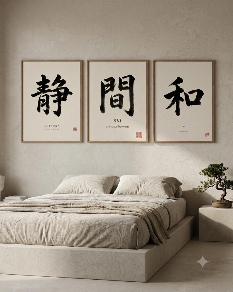 Op de afbeelding: Een set van drie ingelijste kunstprints met lichte houten lijsten. Elke print bevat zwarte Japanse kalligrafie op een cr&egrave;mekleurige achtergrond. De linker print toont SHIZUKA, de middelste ma the space between en de rechter print toont WA Harmony.