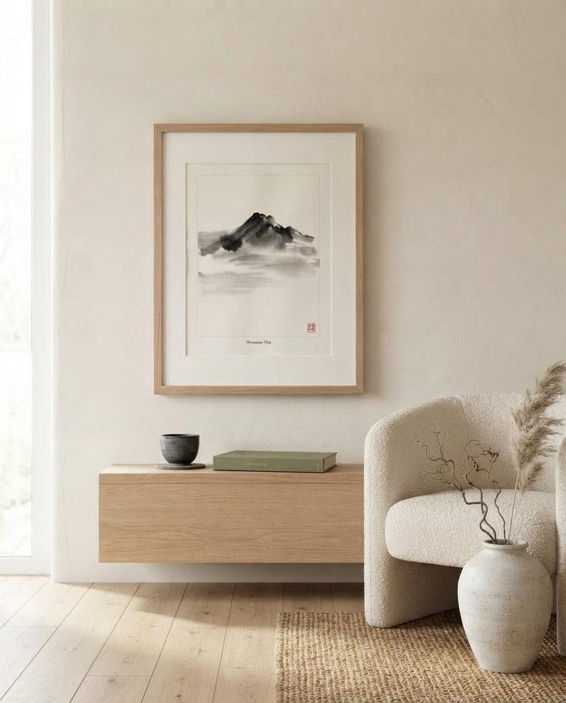 A framed wall art print titled Mountain Mist featuring a black ink wash painting of a mountain peak partially obscured by clouds. The artwork is enclosed in a light-colored wooden frame with a white mat board and a small red seal stamp.
