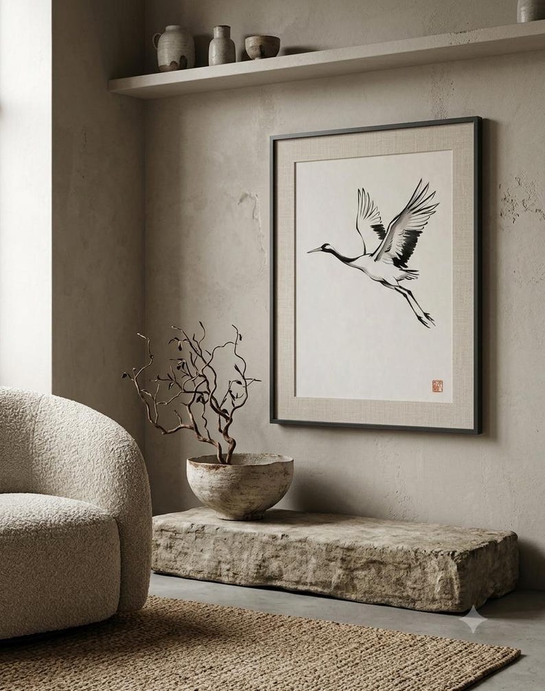 Sumi-e crane print framed in oak, seen on three quiet walls — above a linen bed, on a gallery wall and above an oak console.