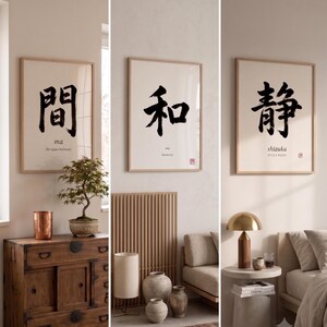 Op de afbeelding: Drie ingelijste wandkunstprints uit de Calm & Oak Japandi Collectie, gelabeld 11-A, 11-B en 11-C. Elke print toont zwarte Japanse kalligrafiekarakters op een cr&egrave;mekleurige achtergrond, met de woorden ma, wa en shizuka eronder gedrukt.