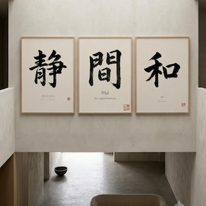 Op de afbeelding: Een set van drie ingelijste wandkunstprints met lichte houten lijsten. Elke print toont grote zwarte Japanse kalligrafiekarakters op een cr&egrave;mekleurige achtergrond. De tekst bevat de woorden SHIZUKA, ma, the space between en harmony.