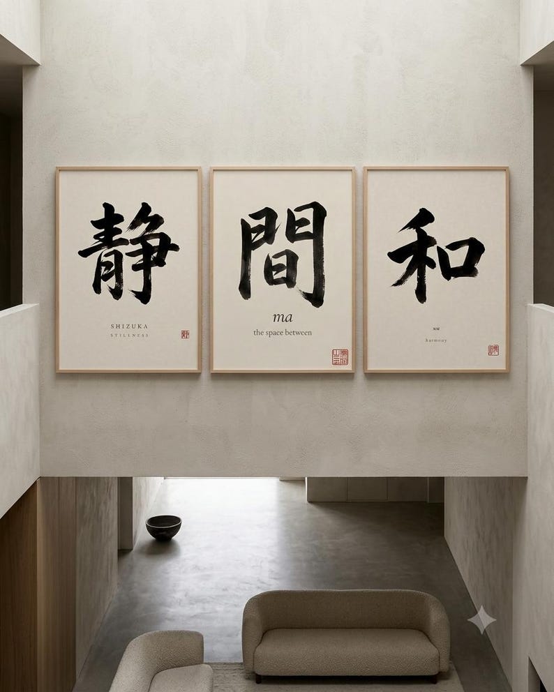 Op de afbeelding: Een set van drie ingelijste wandkunstprints met lichte houten lijsten. Elke print toont grote zwarte Japanse kalligrafiekarakters op een cr&egrave;mekleurige achtergrond. De tekst bevat de woorden SHIZUKA, ma, the space between en harmony.
