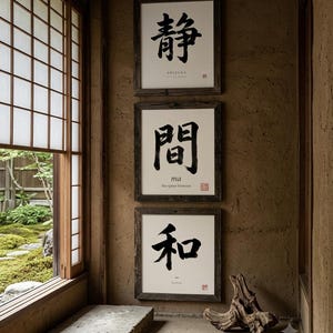 Op de afbeelding: Drie vierkante ingelijste kunstwerken aan de muur met zwarte Japanse kalligrafie op een witte achtergrond. Elke print bevat kleinere Engelse tekst en een rood stempel. De donkerhouten lijsten zijn verticaal aan de muur bevestigd.