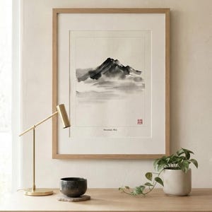 A framed ink wash painting of a mountain landscape in black and gray tones on off-white paper. The artwork features a small red seal stamp and the text Mountain Mist at the bottom, enclosed in a light wood frame with a white mat border.