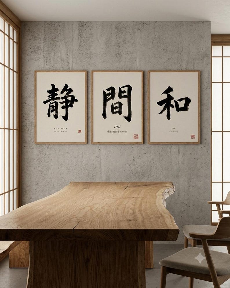 Op de afbeelding: Een set van drie ingelijste wandkunstprints met zwarte Japanse kalligrafie op een cr&egrave;mekleurige achtergrond. Elke print bevat Engelse tekst onder de tekens met de woorden SHIZUKA, ma en wa, samen met een klein rood stempelontwerp.