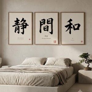 Op de afbeelding: Een set van drie ingelijste kunstprints met lichte houten lijsten. Elke print bevat zwarte Japanse kalligrafie op een cr&egrave;mekleurige achtergrond. De linker print toont SHIZUKA, de middelste ma the space between en de rechter print toont WA Harmony.