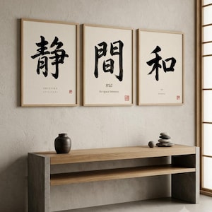Op de afbeelding: Drie ingelijste wandkunstwerken met zwarte Japanse kalligrafie op een gebroken witte achtergrond. De prints tonen de woorden SHIZUKA, ma en wa met hun Engelse vertalingen eronder. Onder de kunstwerken staat een lange houten consoletafel.