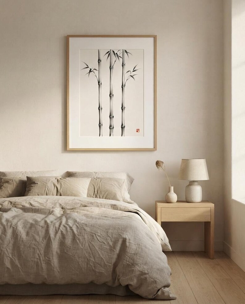 A framed wall art print featuring a black and white ink wash painting of three bamboo stalks. The artwork is displayed in a light wood frame with a white mat border, showcasing detailed nodes and leaves with a small red seal stamp.